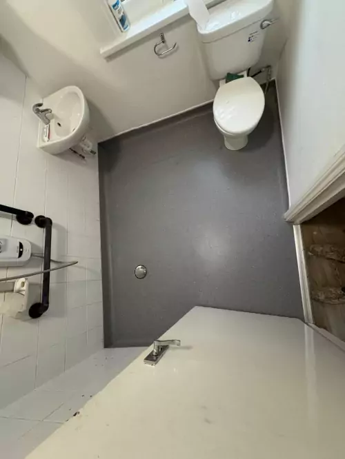 Installation of vinyl flooring in a wet room with a shower, toilet and sink.