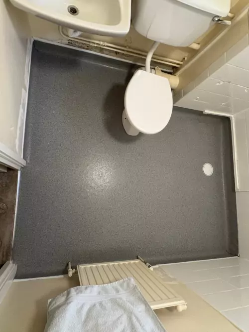 Installation of vinyl flooring in a wet room with a shower, toilet and sink.